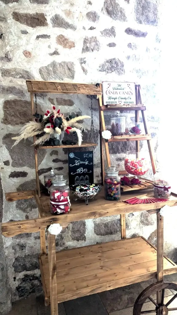 Candy bar vintage en bois avec des bocaux remplis de bonbons colorés, présenté sur un chariot rustique, idéal pour un mariage dans le Var. Décoration avec des fleurs séchées et un panneau en ardoise indiquant 'Candy Bar'. Ambiance champêtre et conviviale, parfaite pour une réception de mariage en extérieur.