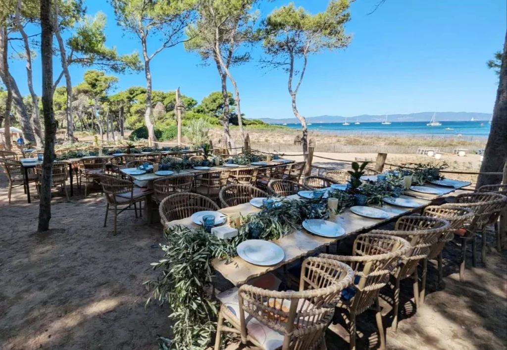 Table de mariage en plein air face à la mer, décorée de guirlandes d’olivier et de vaisselle en céramique dans une ambiance bois naturel et bleu marine. Le noé plage Hyères 83400